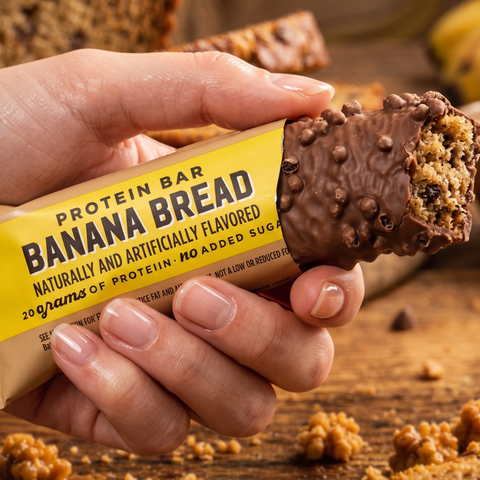 Guiltfree baton proteinowy Barebells Banana Bread w dłoni, nadgryziony, z widocznym wnętrzem i czekoladową polewą.