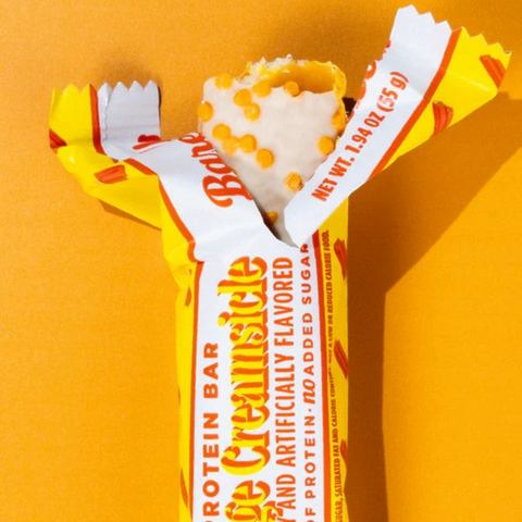 Guiltfree baton proteinowy Barebells Orange Creamsicle w białej polewie z pomarańczową posypką na pomarańczowym tle