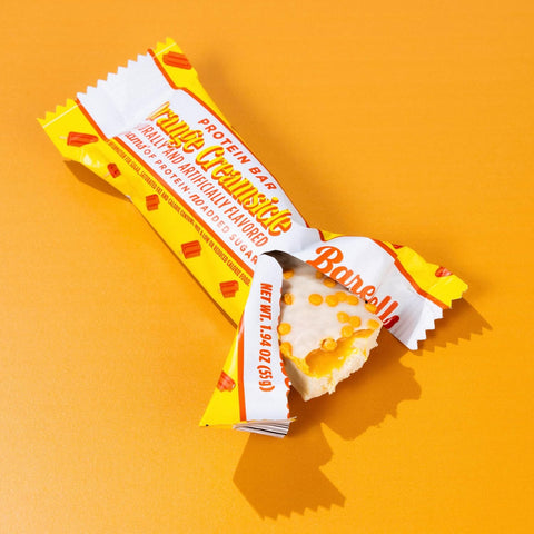 Baton proteinowy Guiltfree Barebells Orange Creamsicle w białej polewie z pomarańczową posypką na pomarańczowym tle