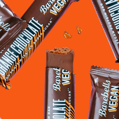 Guiltfree wegański baton proteinowy Barebells o smaku czekolady z pomarańczą w otoczeniu opakowań na różowym tle