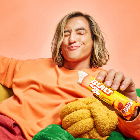 Mężczyzna zadowolony z jedzenia batona proteinowego Guiltfree Built Sour Puff o smaku brzoskwiniowym