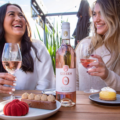Dwie kobiety pijące bezalkoholowe wino różowe Giesen 0% Rosé przy stole z deserami na zewnątrz.