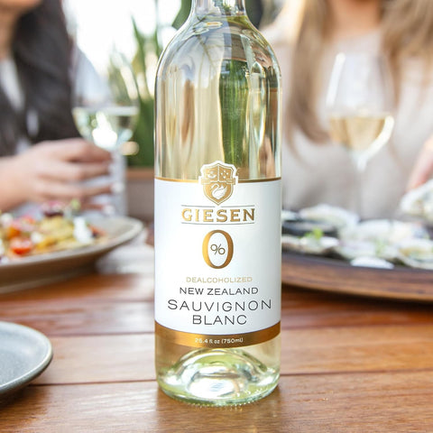Butelka bezalkoholowego wina Guiltfree Giesen Sauvignon Blanc 0% na drewnianym stole w otoczeniu przekąsek