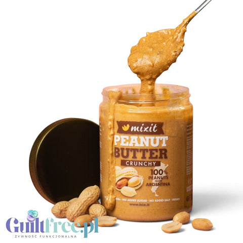 Guiltfree Mixit masło orzechowe crunchy z kawałkami orzechów w słoiku z łyżką na różowym tle