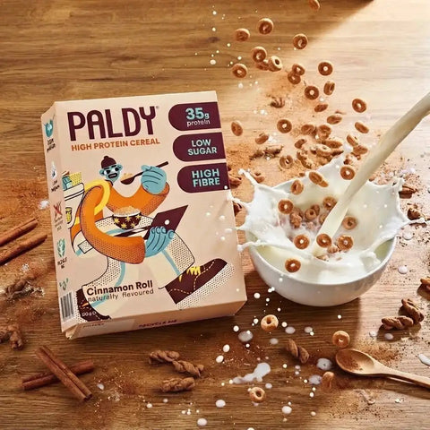Guiltfree Paldy Cinnamon Roll proteinowe płatki śniadaniowe wpadające do miski z mlekiem na drewnianym stole