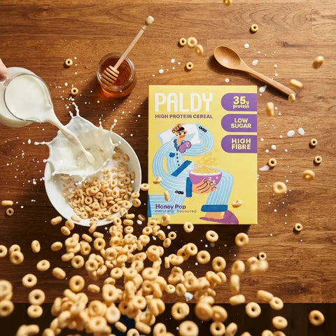 Guiltfree Paldy Honey Pop proteinowe płatki śniadaniowe w kształcie kółeczek z mlekiem wpadającym do miski na stole