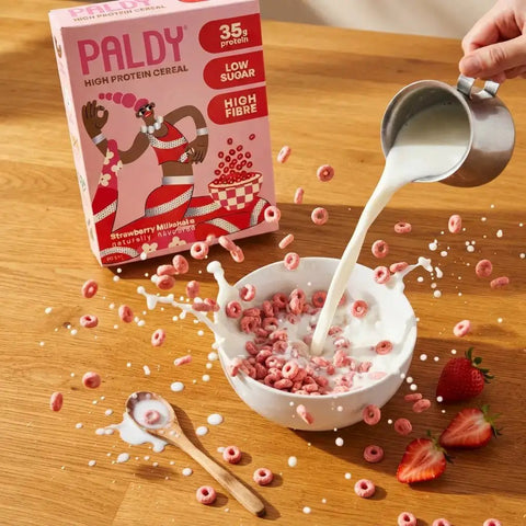 Guiltfree Paldy Strawberry Milkshake proteinowe płatki w różowe kółeczka wpadające do miski z mlekiem na drewnianym stole