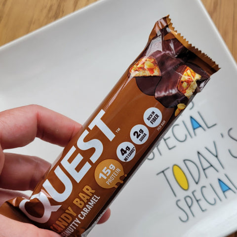 Guiltfree Quest Nutrition Peanutty Caramel protein candy bar in hand, showing chocolate, caramel, and peanut layers.